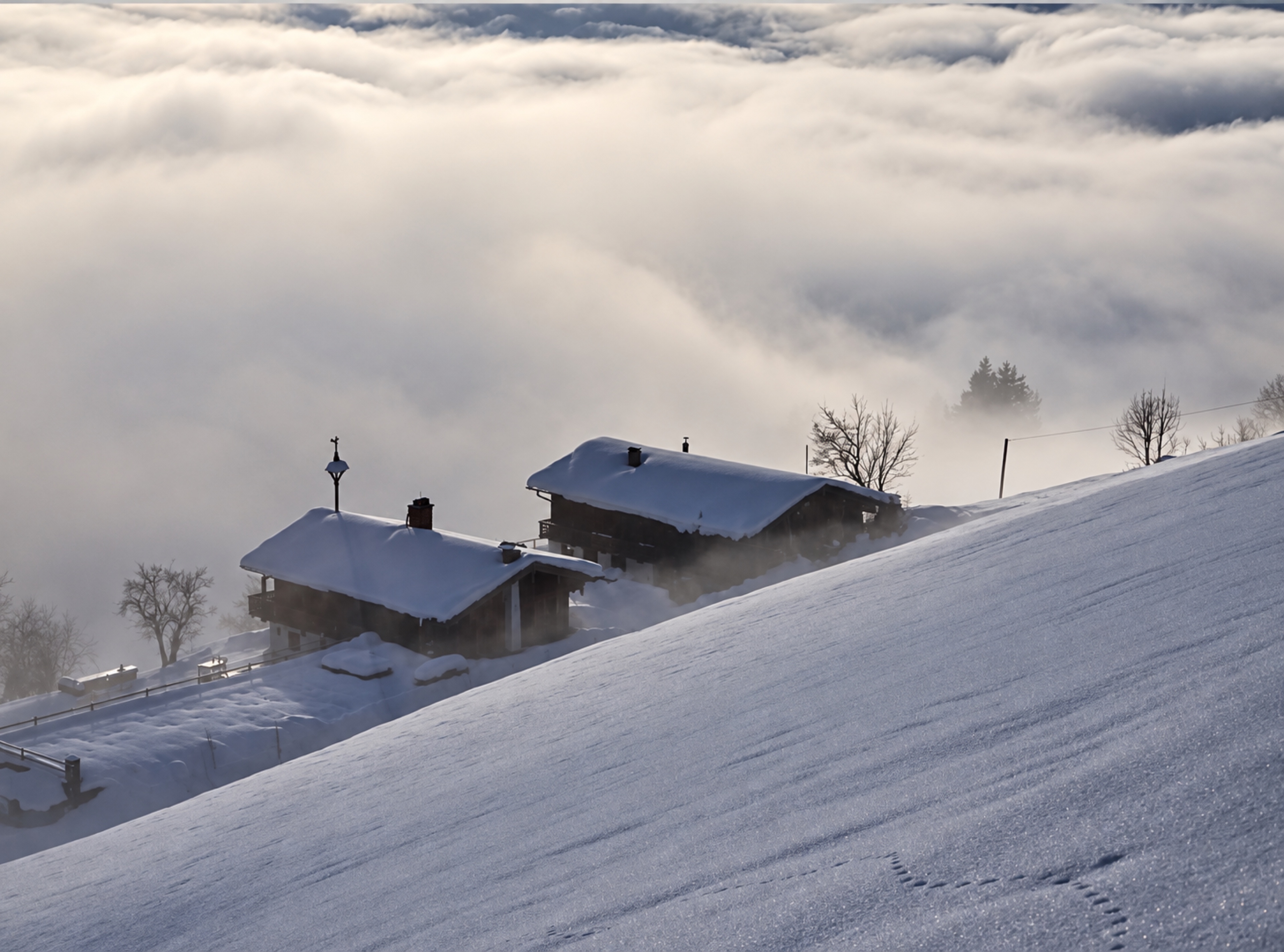 Verschneite Gebäude am Hang über einem weiten Nebelmeer im warmen Winterlicht.